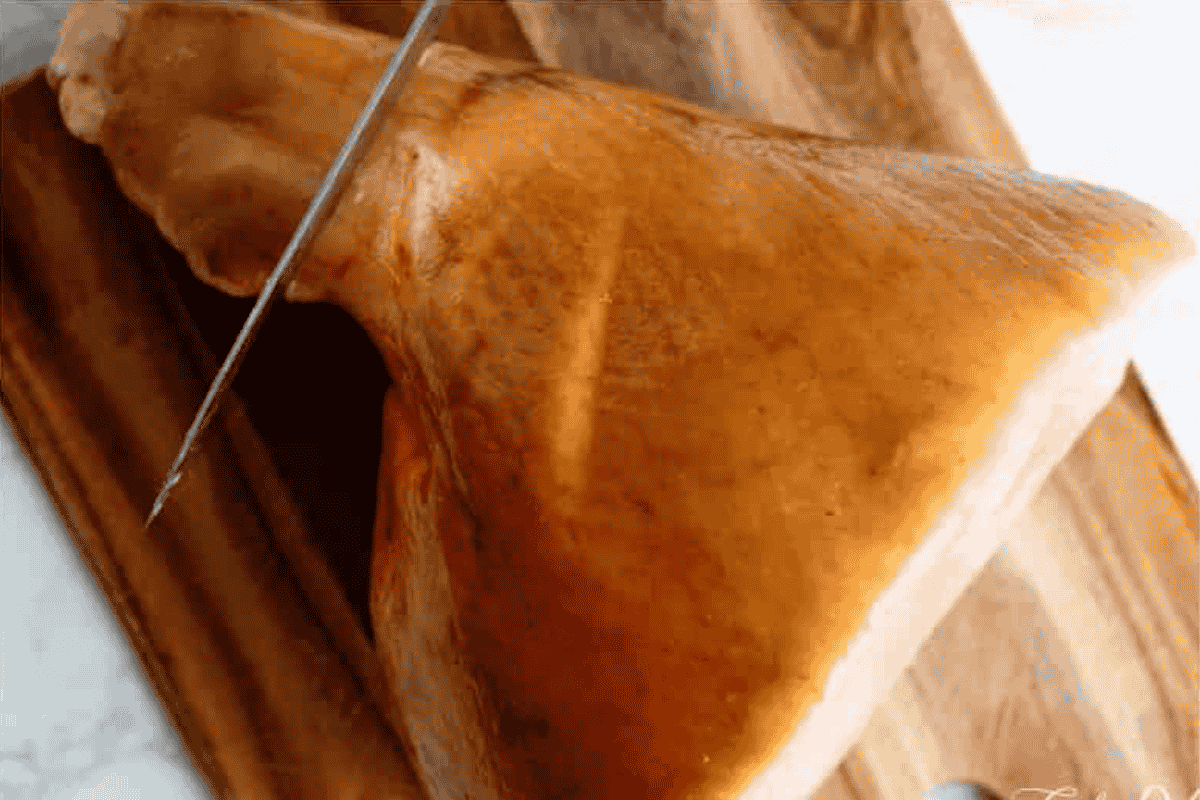 a top view of ham showing rind on and a knife cuttin the top of the bone area