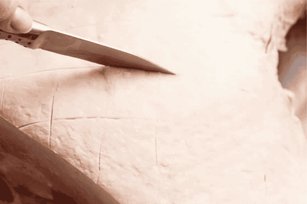 a knife scoring the fat of the leg ham in a diamond pattern 1 inch thick and 1/4 inch deep.