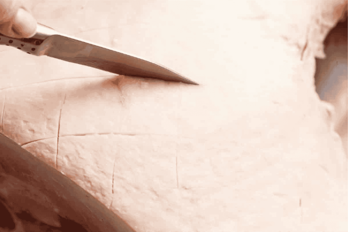 a knife scoring the fat of the leg ham in a diamond pattern 1 inch thick and 1/4 inch deep.