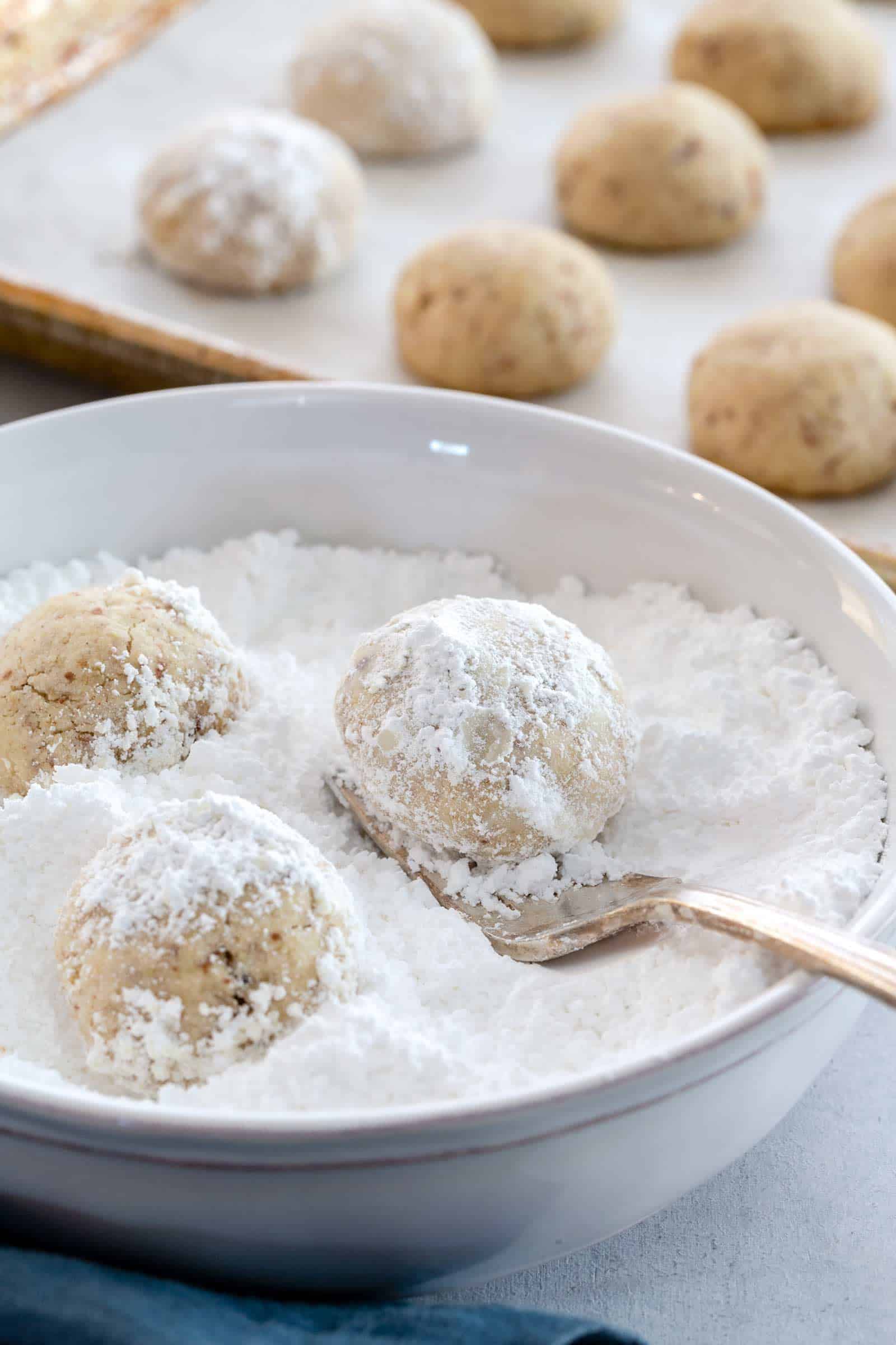 in process shot of covering snowball cookies with powdered sugar