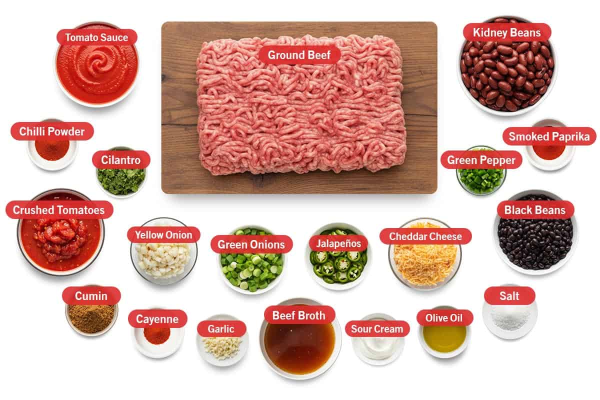 Top shot of ingredients: tomato sauce, chilli powder, cilantro, crushed tomatoes, yellow onion, green onions, Jalapeños, cheddar cheese, black beans, cumin, cayenne, garlic, beef broth, sour cream, olive oil, salt, ground beef, kidney beans, green pepper, and smoked paprika.