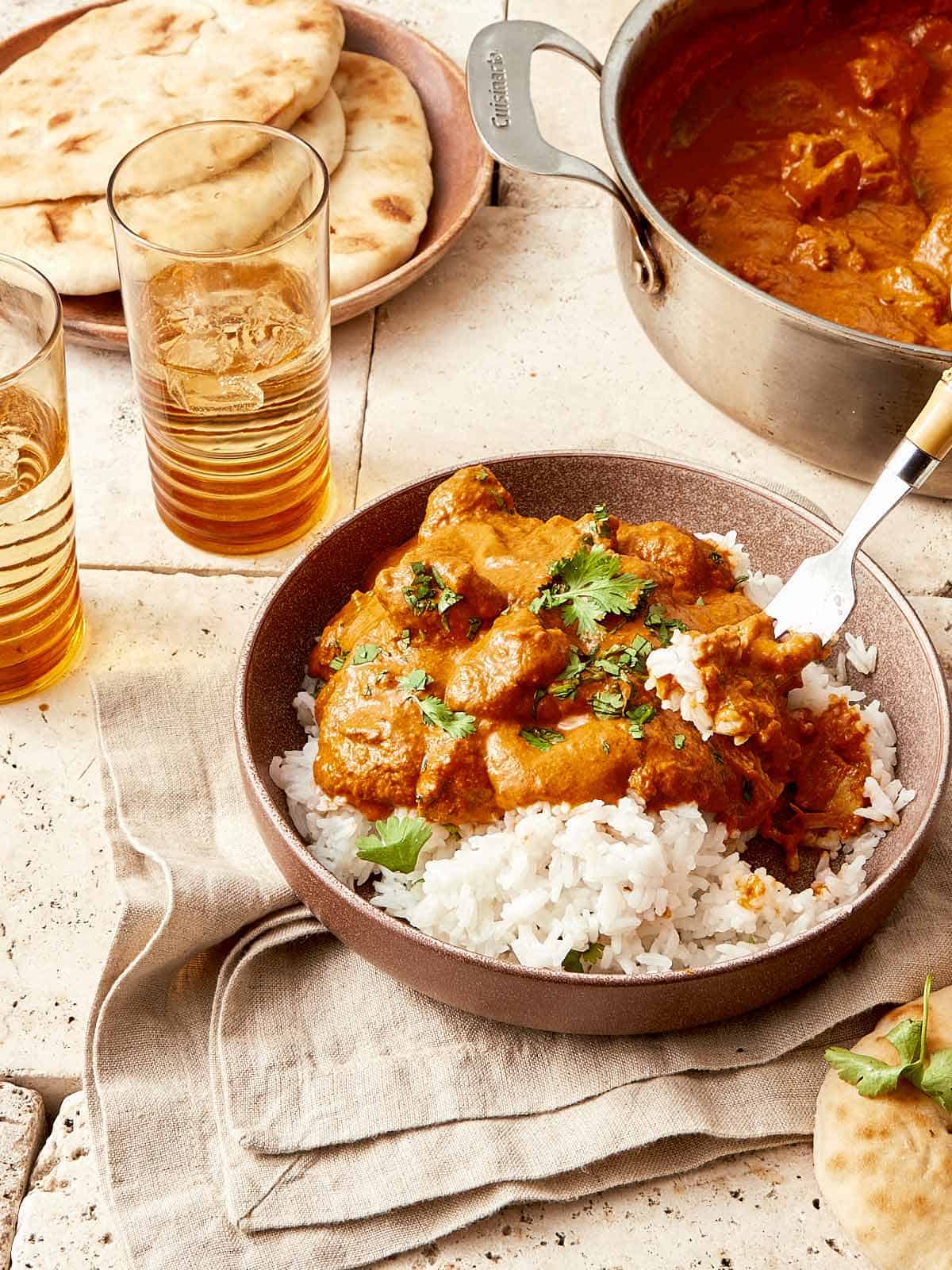 Butter Chicken on a bed of rice, with tandoori roti being scooped up by a silver fork.