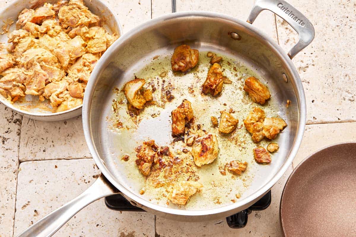 chicken dice being fried in a large skillet with oil.
