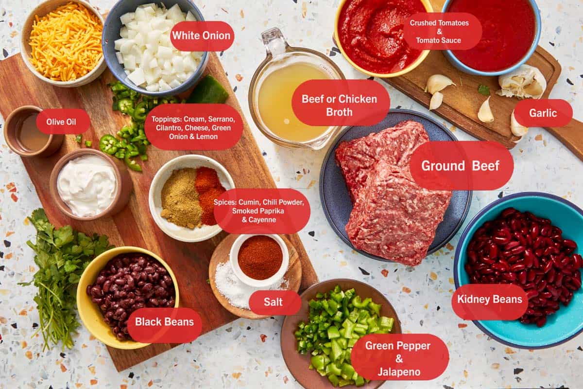 Top shot of ingredients: tomato sauce, chilli powder, cilantro, crushed tomatoes, yellow onion, green onions, Jalapeños, cheddar cheese, black beans, cumin, cayenne, garlic, beef broth, sour cream, olive oil, salt, ground beef, kidney beans, green pepper, and smoked paprika.