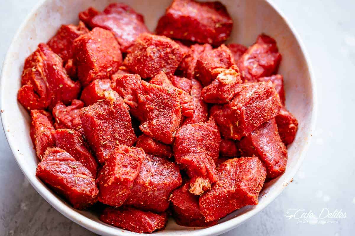 How to make steak bites. Marinating seasoned diced steak pieces in a white bowl against a light grey background | cafedelites.com