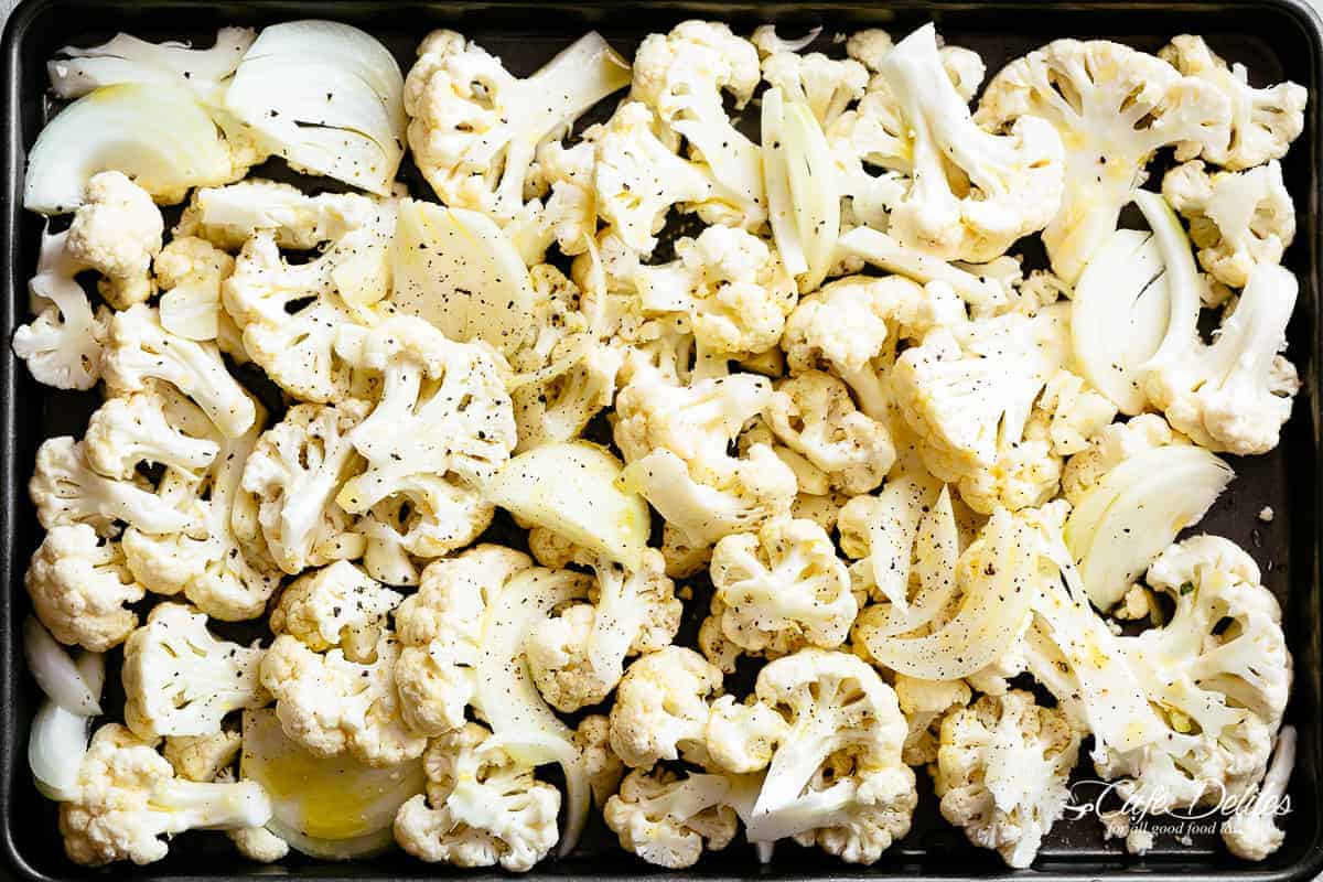 Uncooked cauliflower on a baking tray with large chunks of onion. 