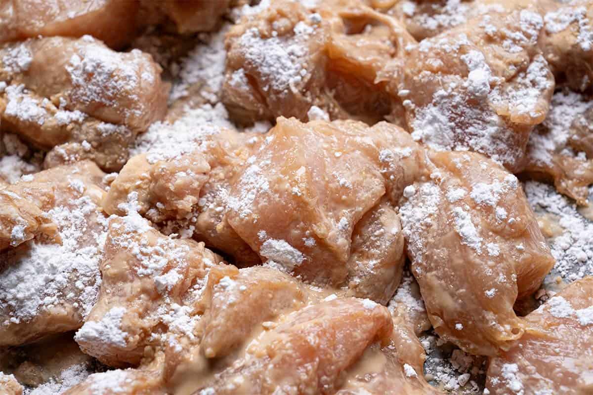 marinated chicken being coated with cornstarch very close up