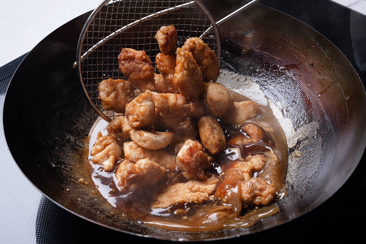 honey marinade in a wok with fried chicken pieced being poured in