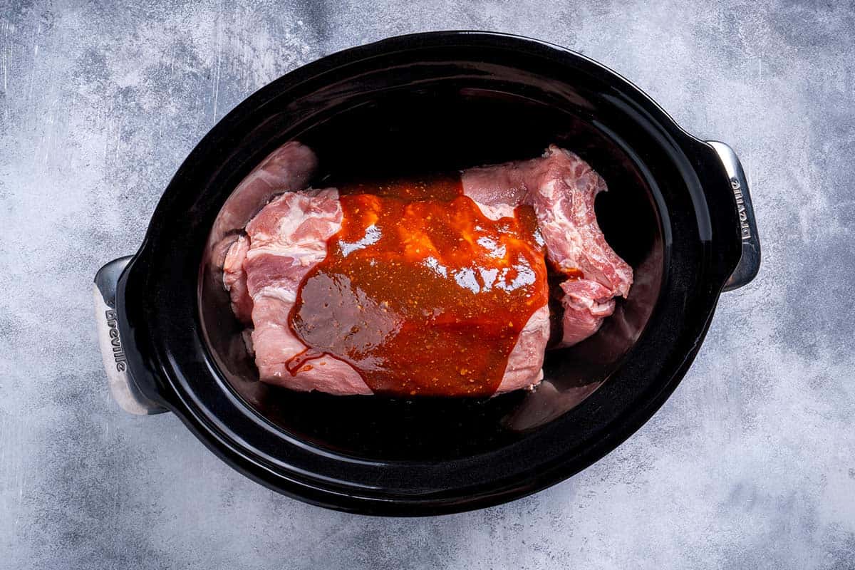 baby back ribs inside the slow cooker with barbecue sauce mixture poured on top 