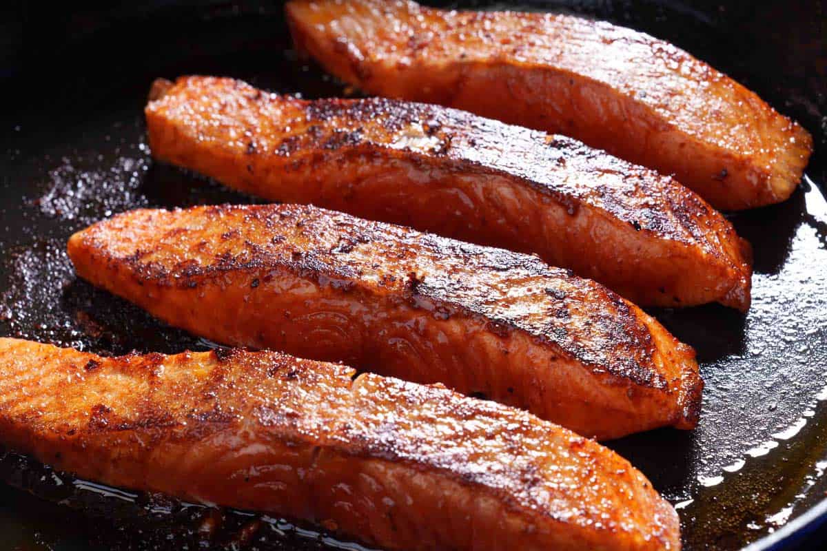 Image of the salmon being seared in a skillet and cooked on both sides to achieve a perfect, nice crust.