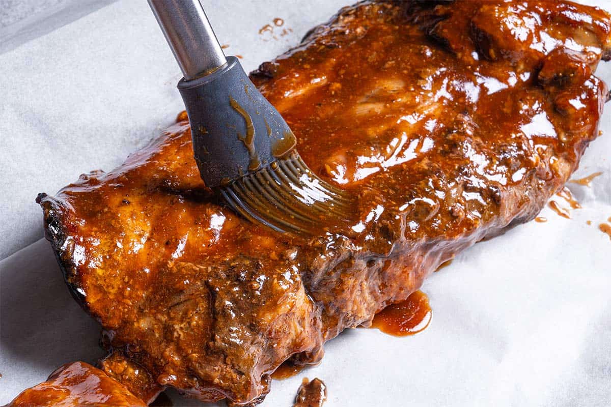 Rack of ribs being glazed with barbecue mixture on a baking tray 