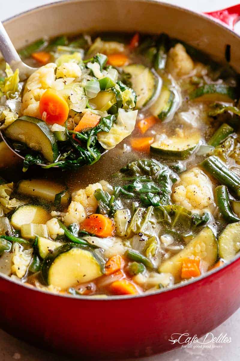 A ladle scooping vegetable soup from a large pot. 