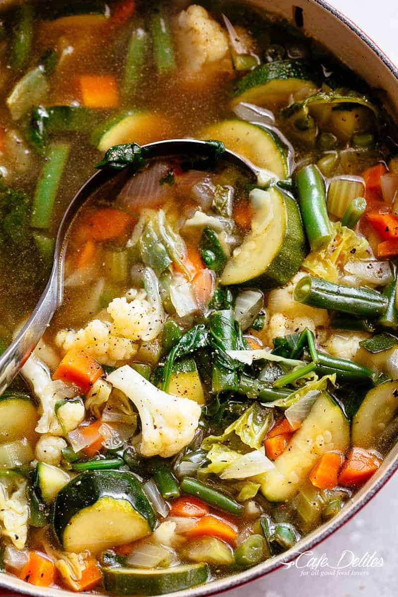 Close up of vegetable soup being stirred with a large spoon. 