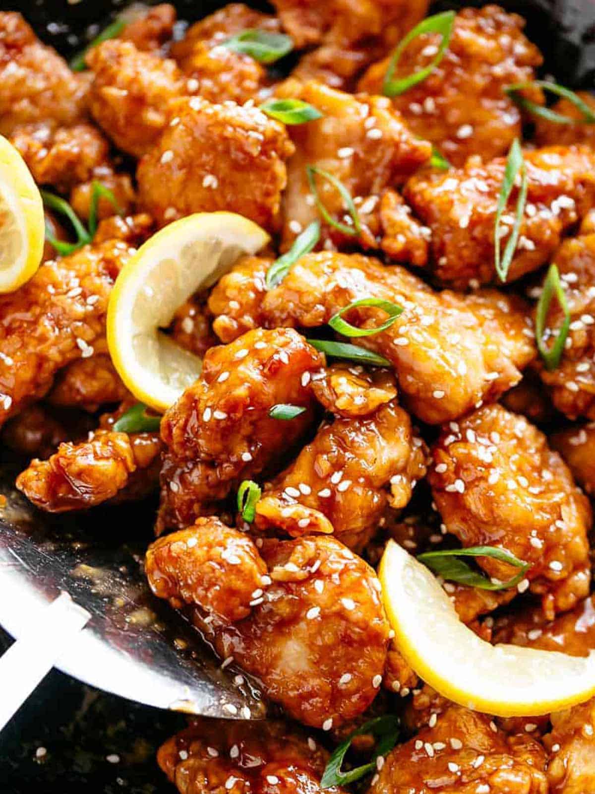 Chicken bites with a sticky, sweet and sour, Chinese lemon sauce, sprinkled with sesame seeds and sliced spring onion in a pan