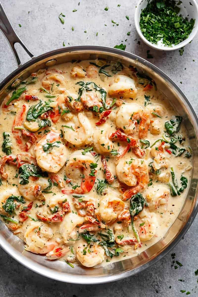 Creamy Garlic Butter Tuscan Shrimp coated in a light and creamy sauce filled with garlic, sun dried tomatoes and spinach in a pan.