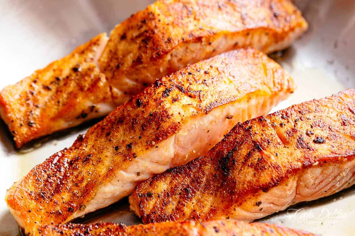 Four salmon fillets searing in a pan. 