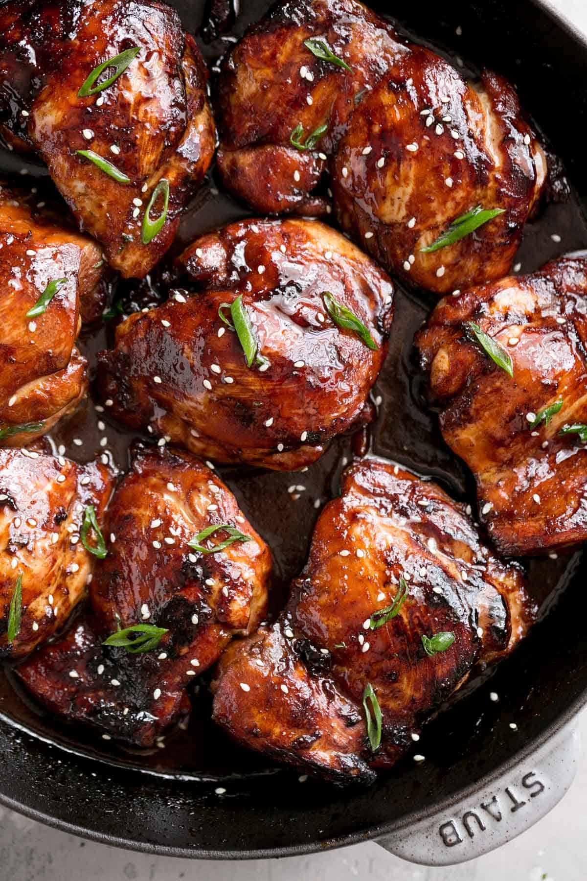 Close-up top view of honey soy baked chicken thighs in a black skillet, roasted in the oven and glazed in a dark sauce.