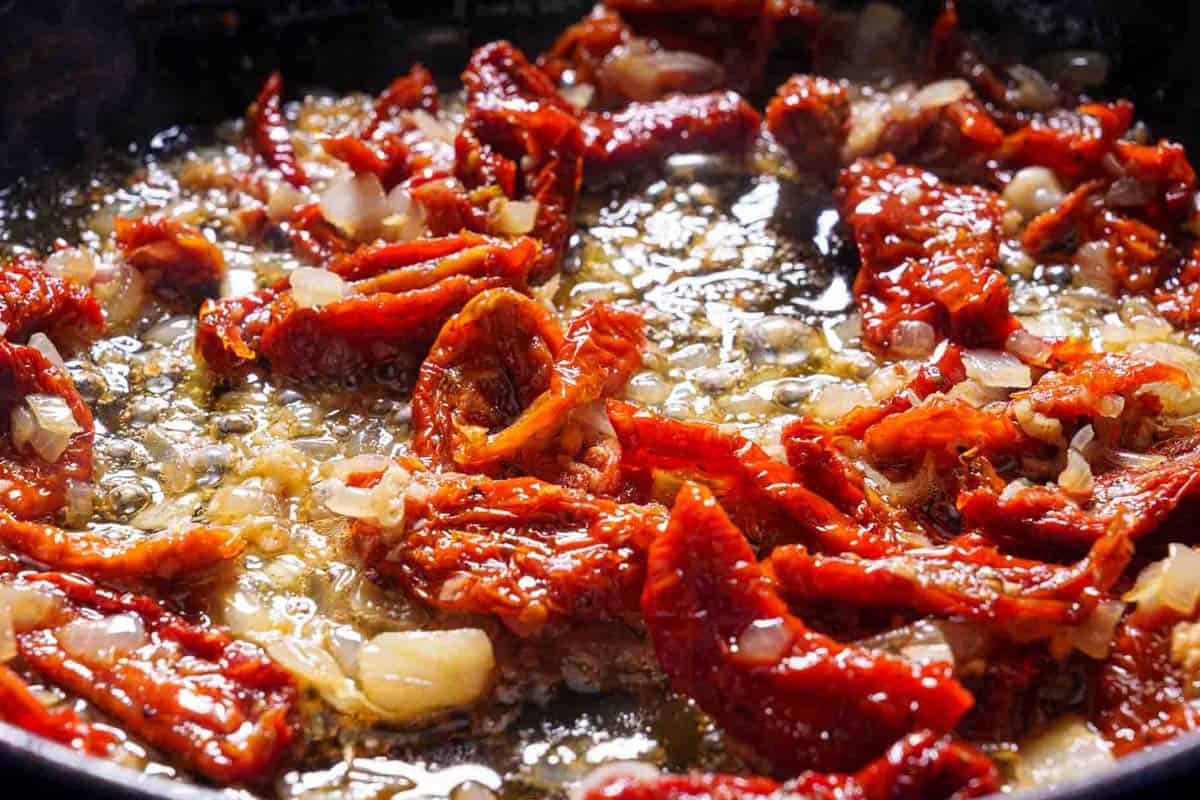 Image of onions being fried with butter and dried tomatoes, accompanied by white wine.