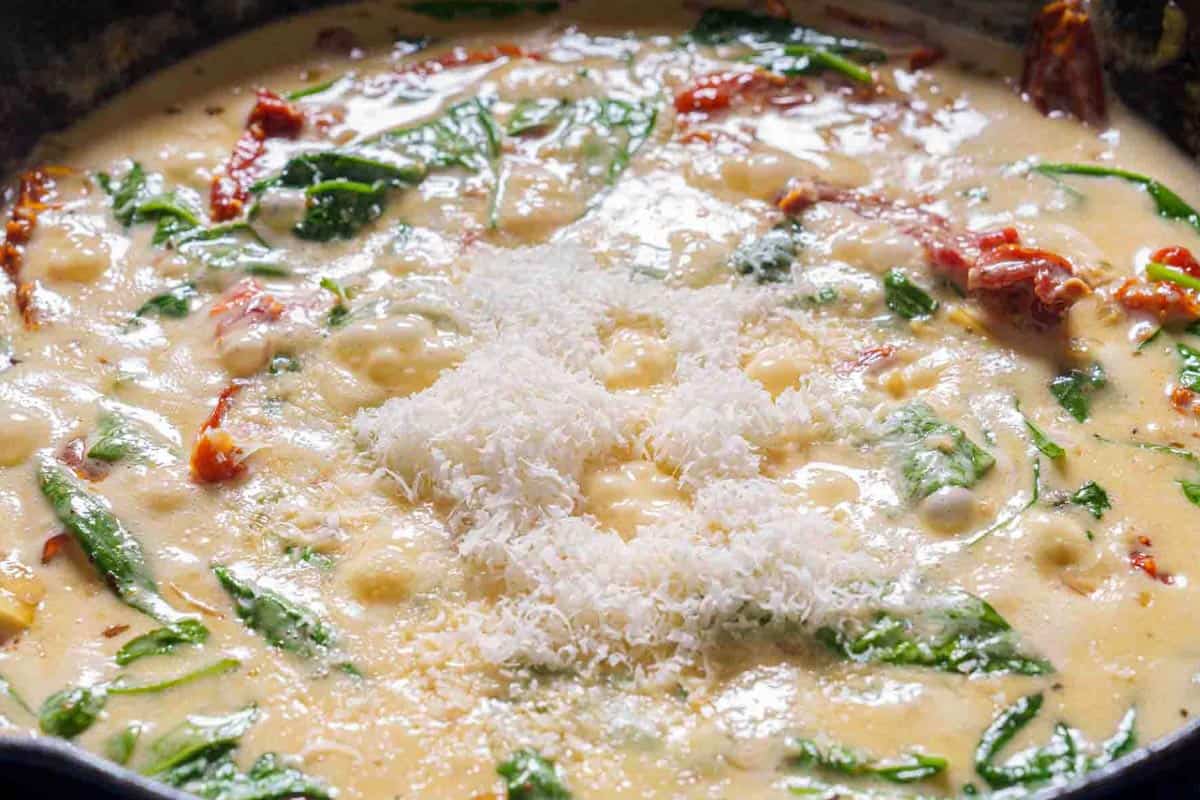 An image shows spinach and cheese being added to the mixture to create the sauce.