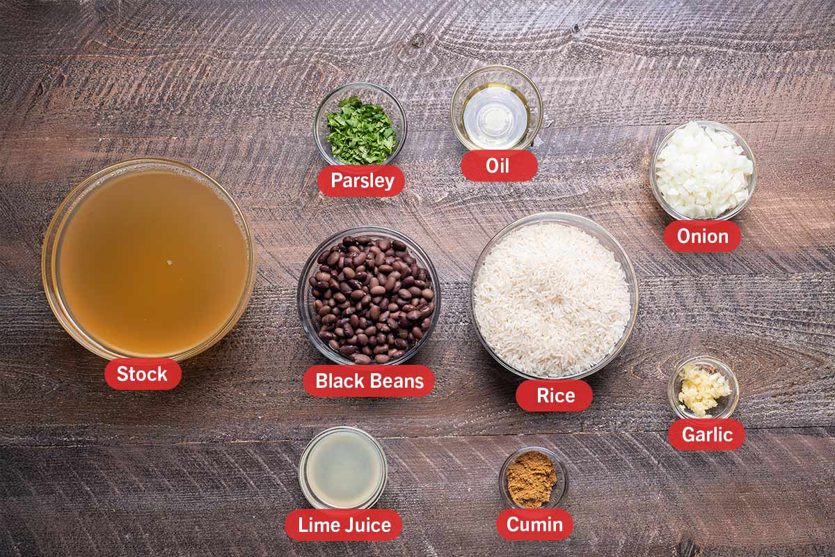 ingredients laid out from a top view and labelled against a woodgrain backdrop, Stock, Parsley, oil, onion, black beans, rice, lime juice, cumin, garlic