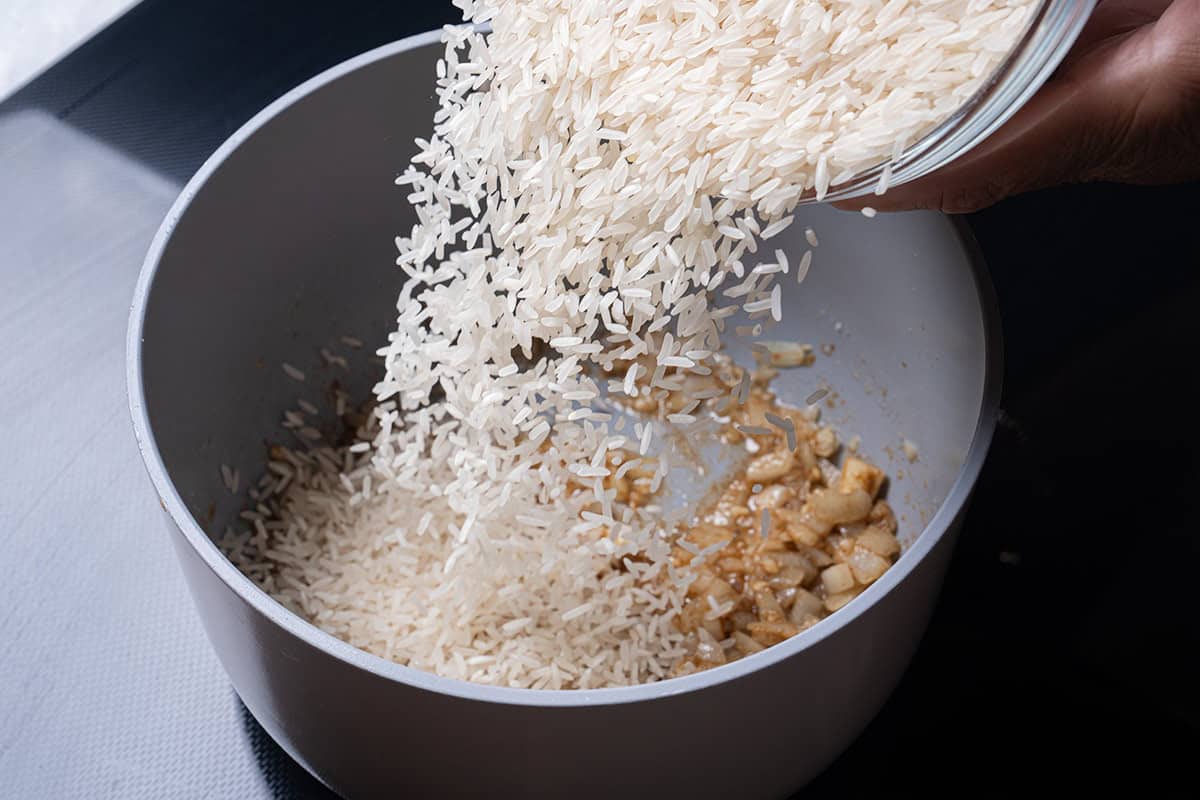 Garlic and cumin heated in a pan with rice being poured in