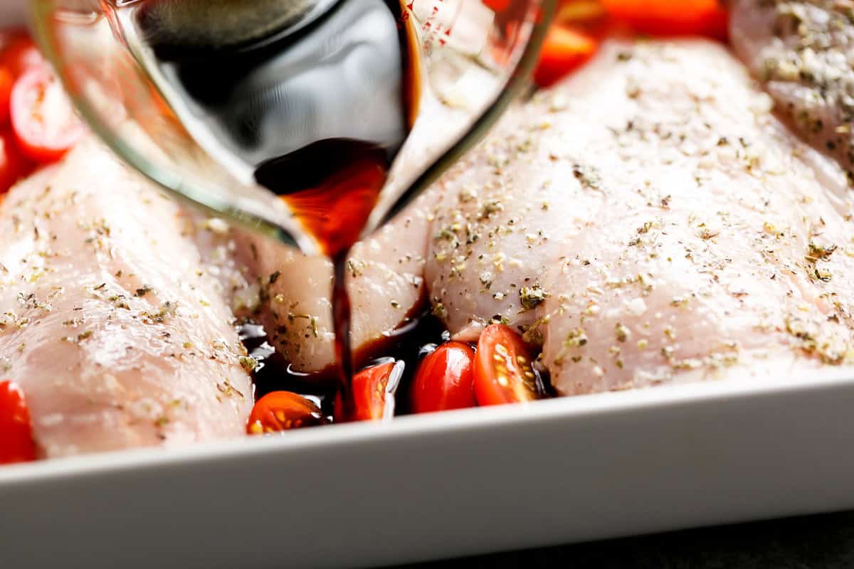 Pouring the balsamic glaze into the raw chicken before baking