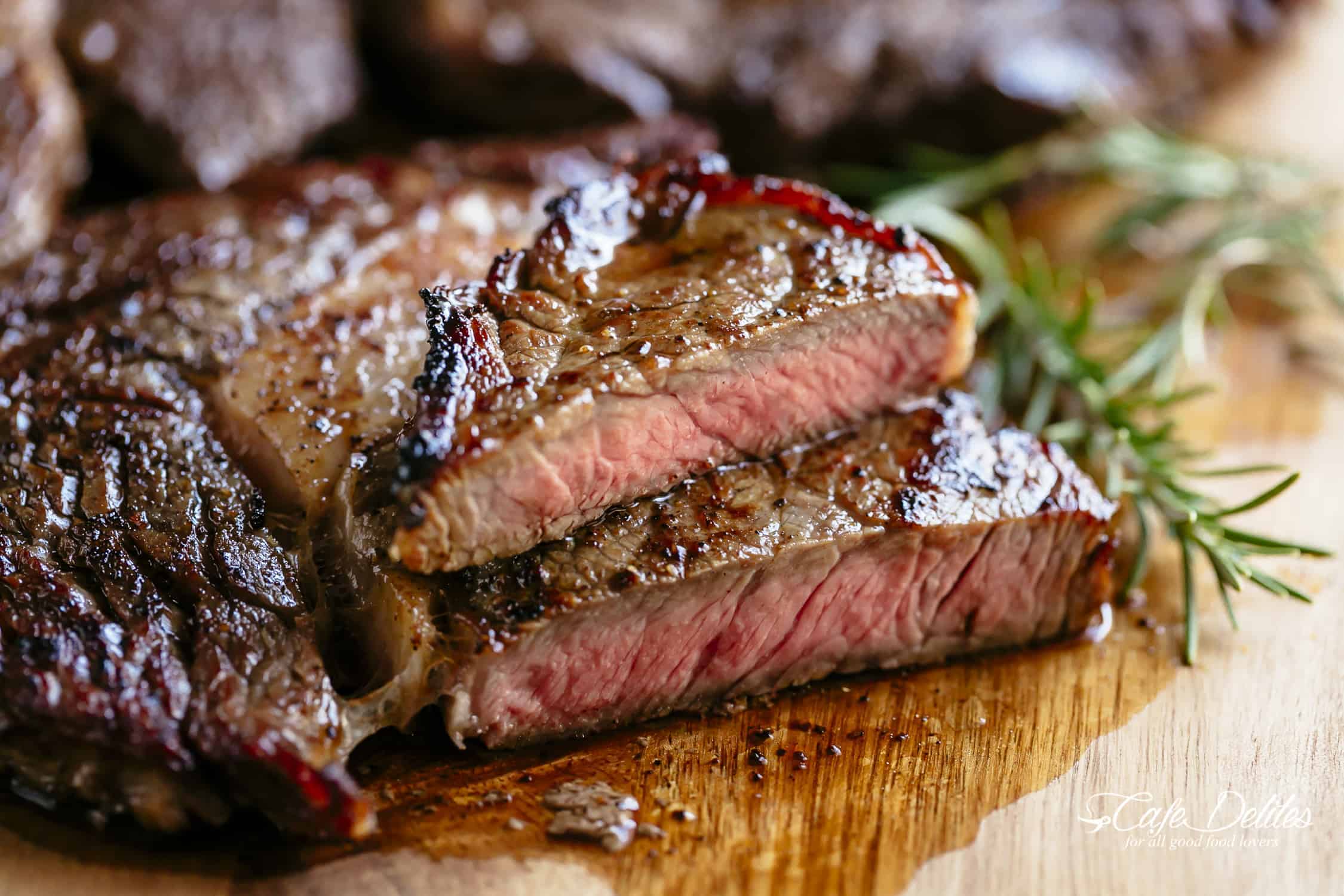 Side view of sliced, medium rare steak on a wood chopping bored and a stick of rosemary.