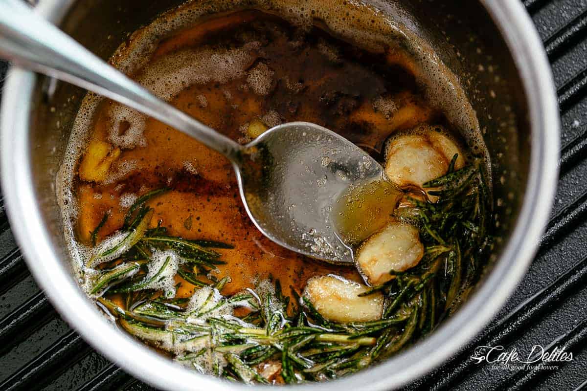 Browned butter with garlic cloves and sprigs of rosemary in silver pot on a grill pan.