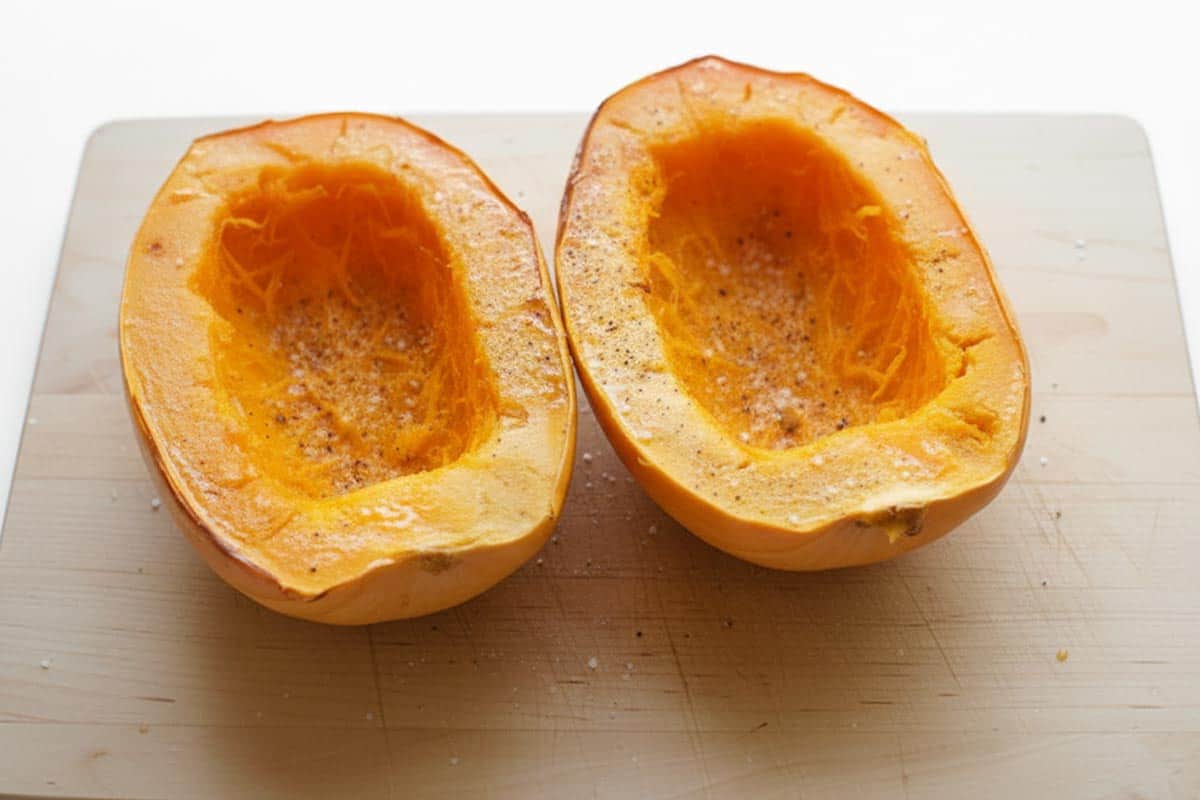 Squash cut in half on a cutting board and brushed with olive oil and sprinkled with salt and pepper.