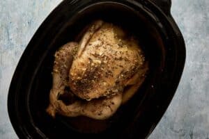 Seasoned whole turkey placed inside slow cooker on herb base