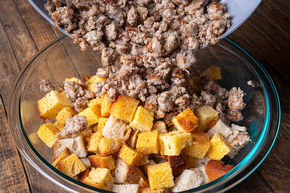 cut up cornbread in a clear bowl with cooked pork sausages being poured in