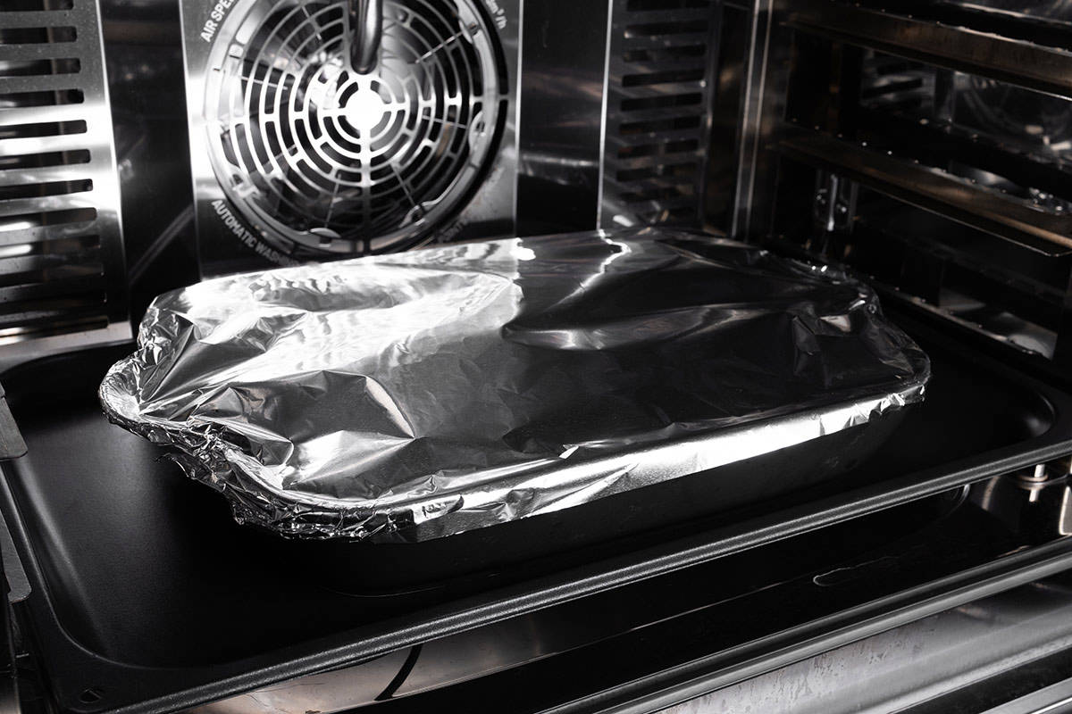 cornbread dressing in the oven in a baking dish covered with foil