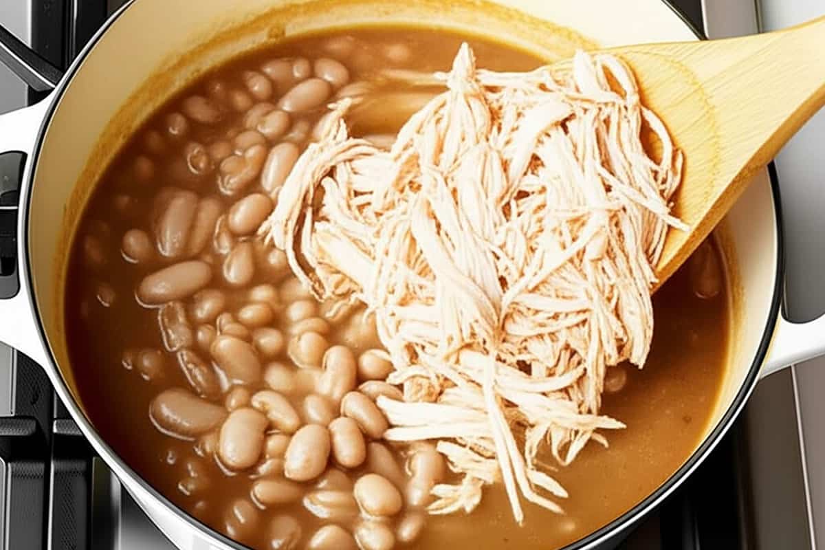 Shredded turkey and white beans with stock in a pot.