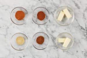 transparent bowls with sugar, paprika, chili, herbs, salt, garlic powder, onion powder, and pepper.