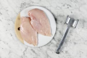 raw chicken with a meat mallet in the side