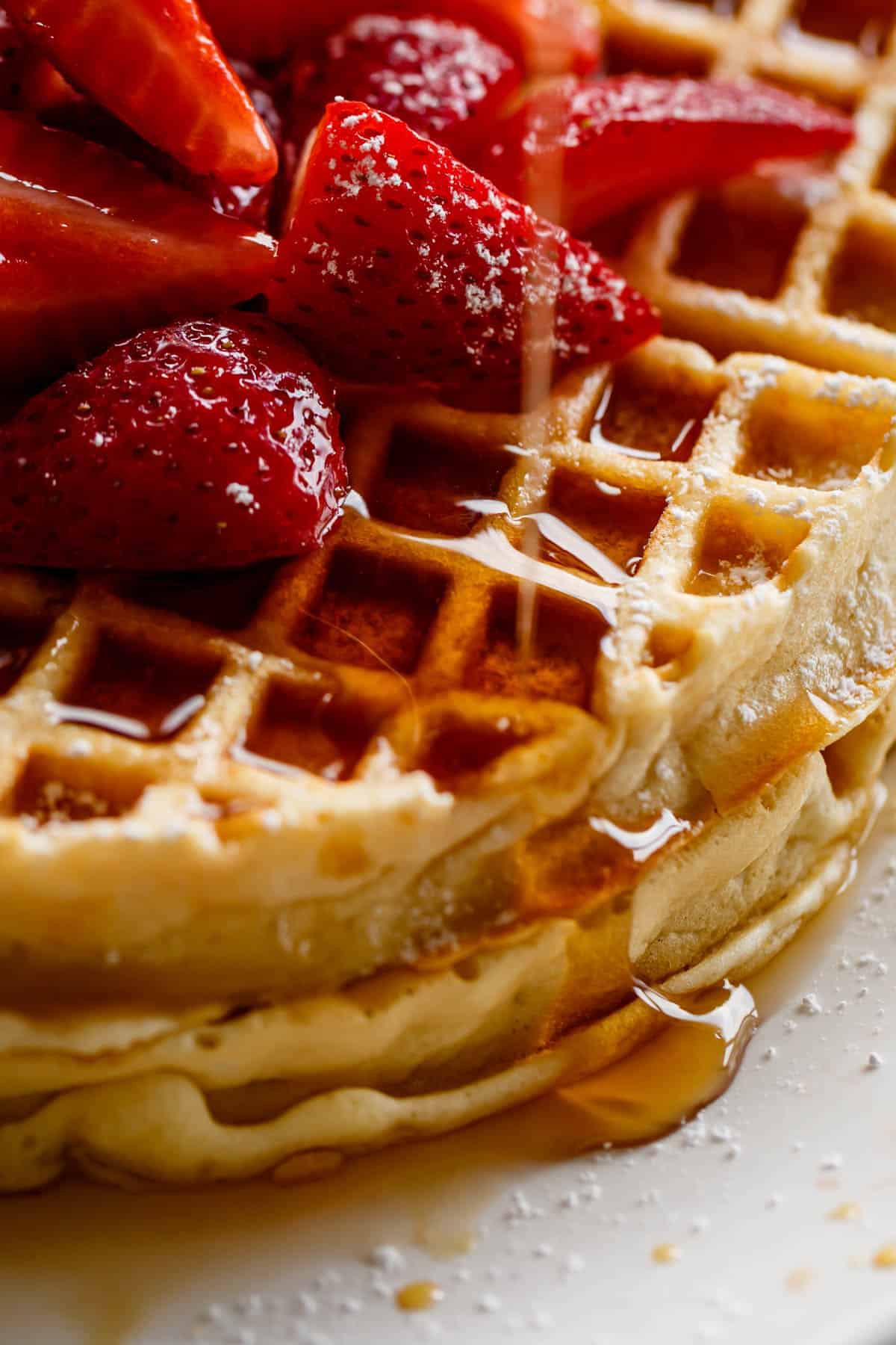 Close up of maple syrup being drizzled over a piled of chopped strawberries. 