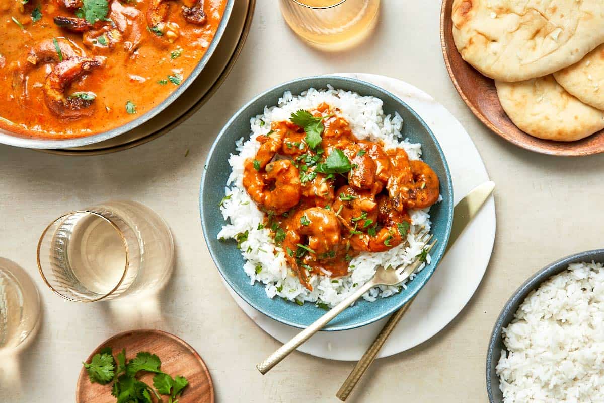 A dining table displaying vibrant bowls of curry alongside bowls of fluffy rice, ready to be served with warm naan.