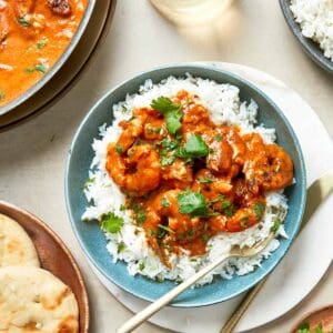 A plate of Coconut Shrimp with rice, bread and curry.