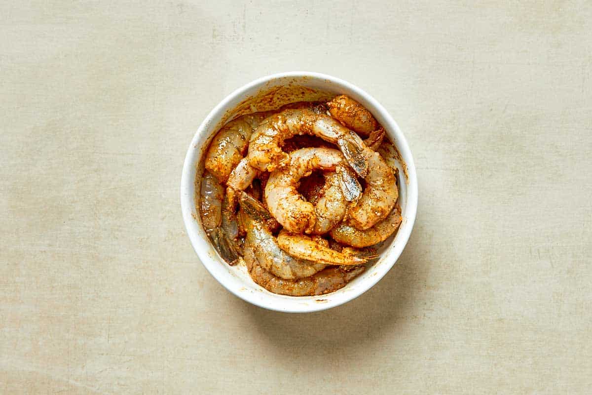 A bowl of shrimp served in a white dish, placed on a wooden table.