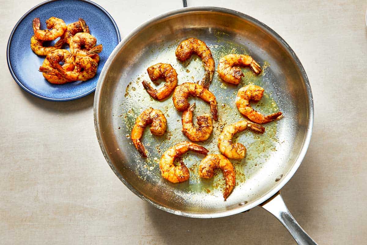 A frying pan with shrimp beside a colorful plate of food, showcasing a delicious meal.