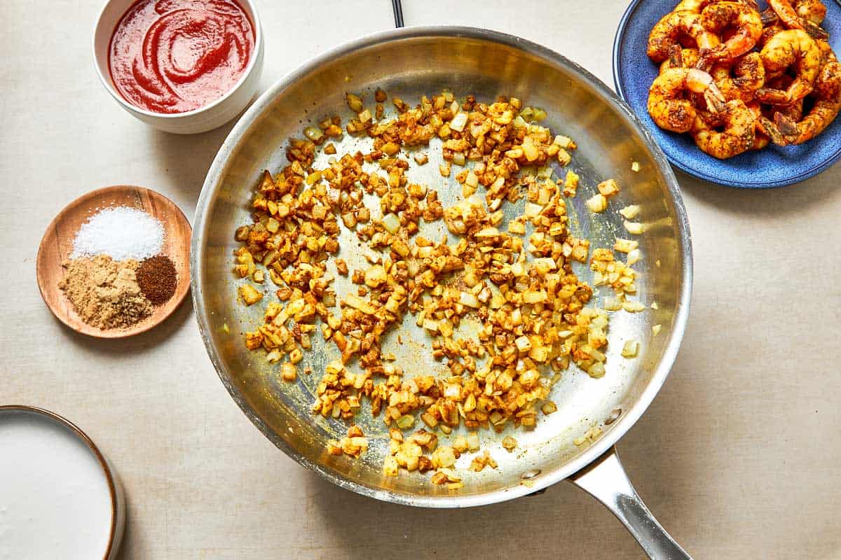 A skillet filled with golden onion, and other colorful ingredient