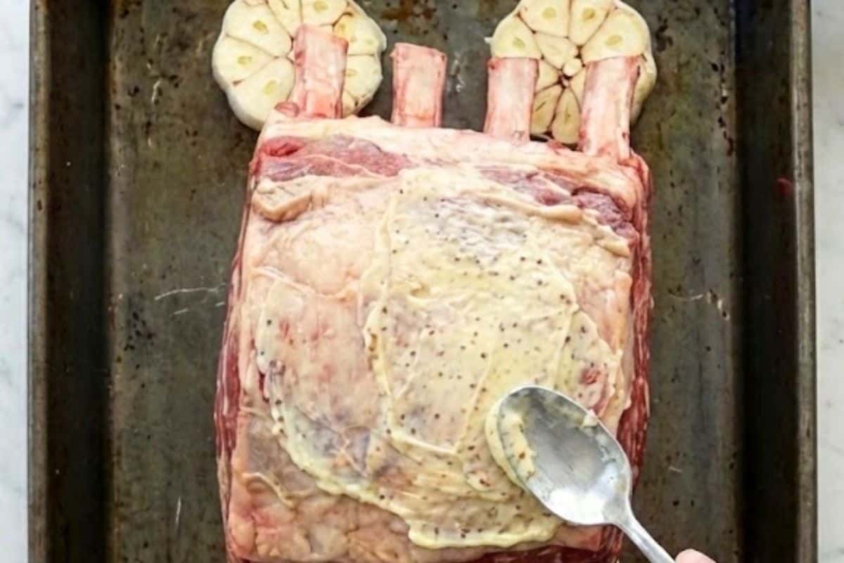 Arrange the garlic heads cut-side up in a roasting pan. Spread garlic butter on the bone side of the roast and place it on top of the garlic halves. - 6