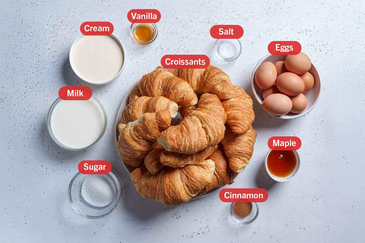 Image of the ingredients needed for this recipe, specifically: croissants, salt, eggs, maple syrup, cinnamon, sugar, milk, cream, and vanilla.