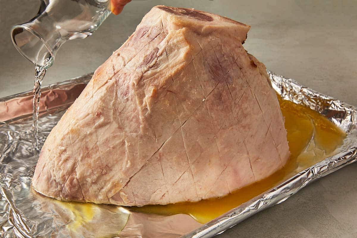 A person is seen pouring water over a large ham, readying it for the cooking process.