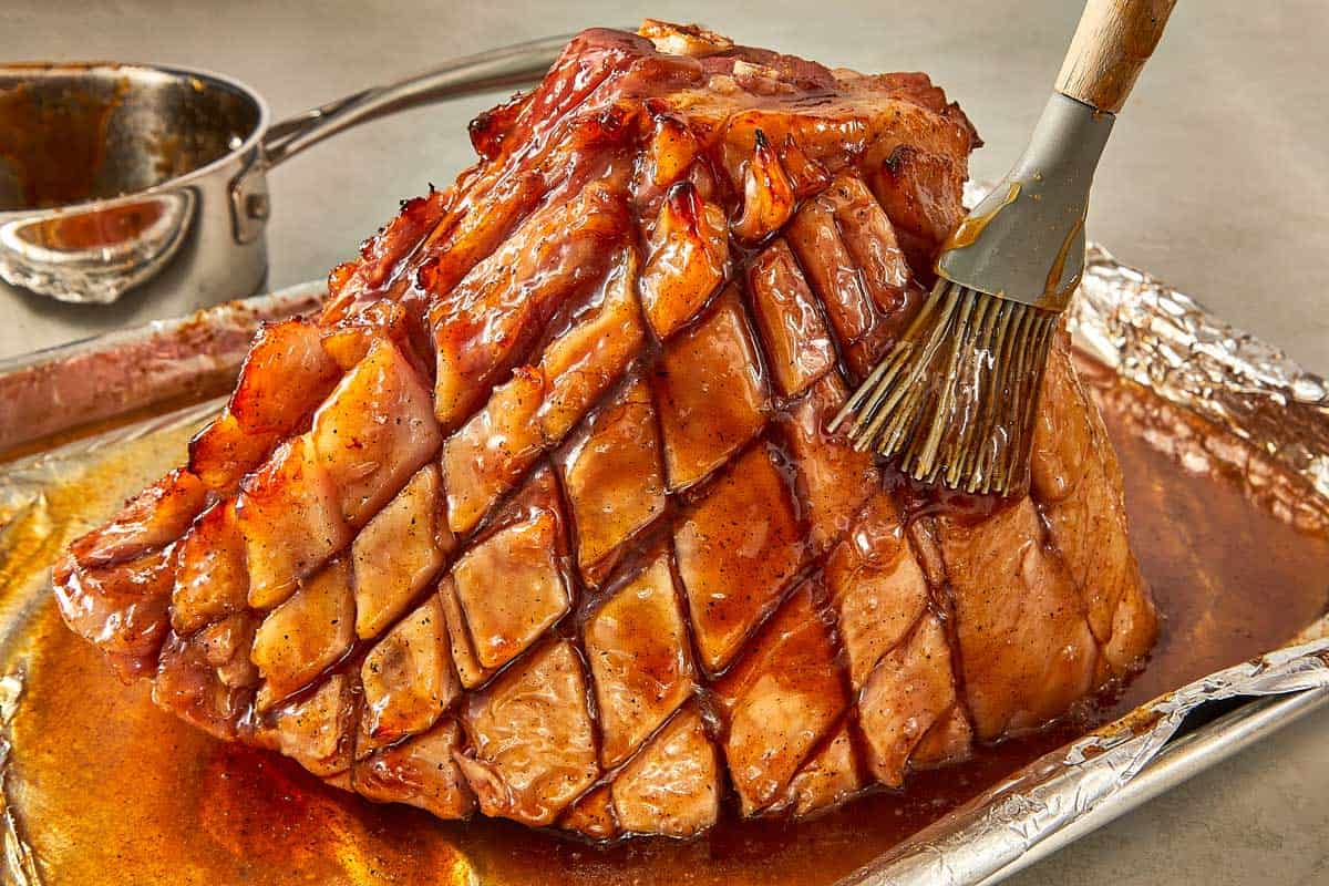 A baking sheet holds a maple ham, glistening with a rich glaze as it cooks in the oven.