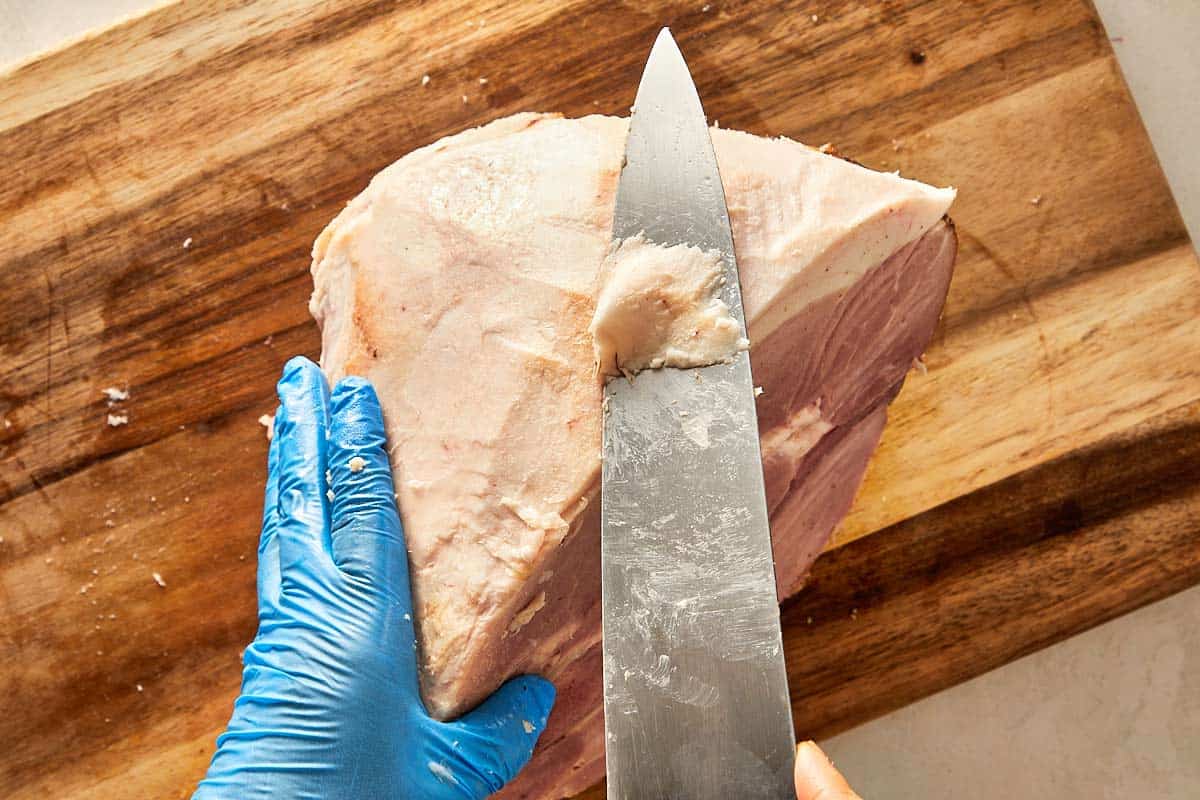 cutting the bone ham with a knife revealing the fat layer underneath the rind