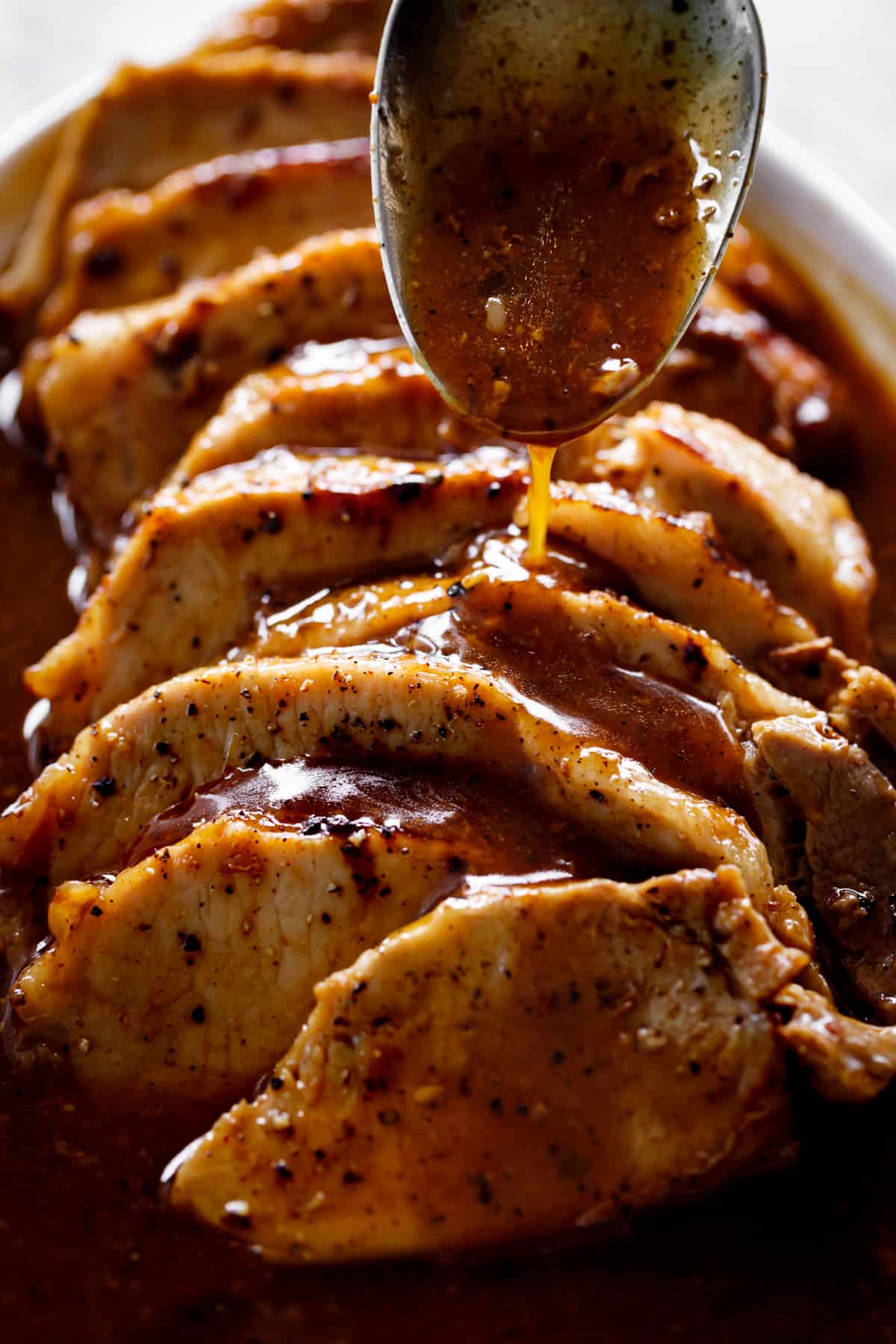 Honey garlic sauce being drizzled over the best pork loin roast with a silver metal spoon | cafedelites.com