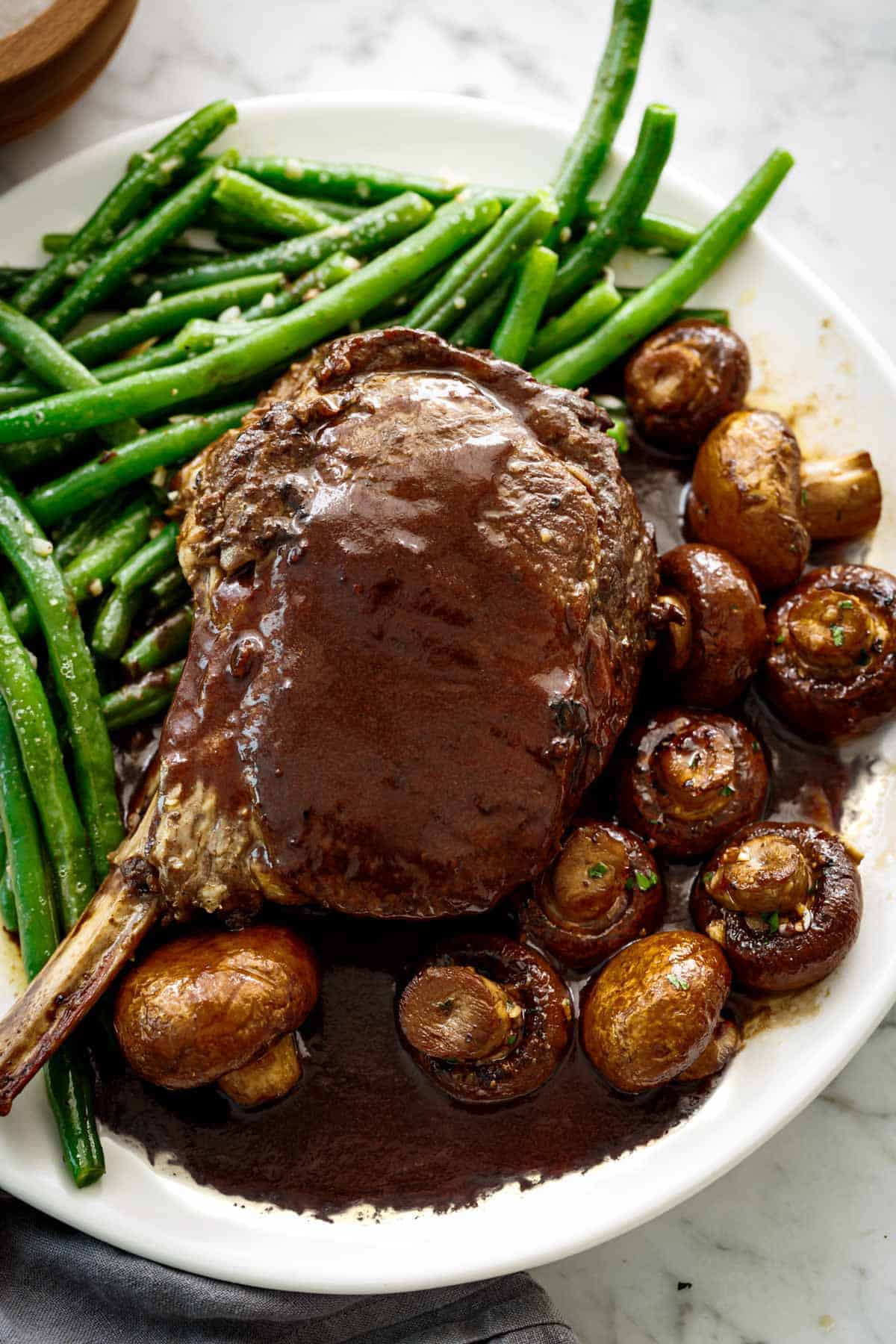 Sautéed Buttery Green Beans plated as a side with a juicy prime rib and balsamic soy roasted mushrooms.