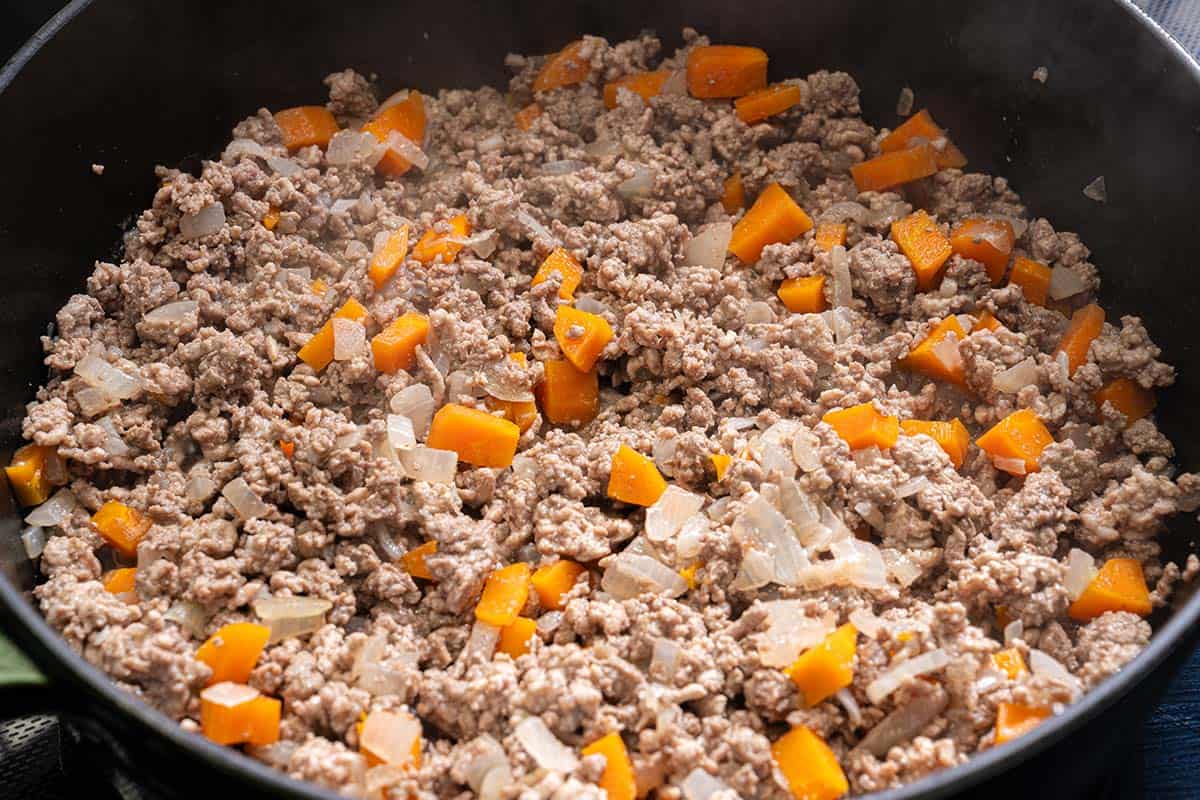 mage of ground meat being sautéed with onions and carrots in a pot, showing a mix of browned meat and softened vegetables.