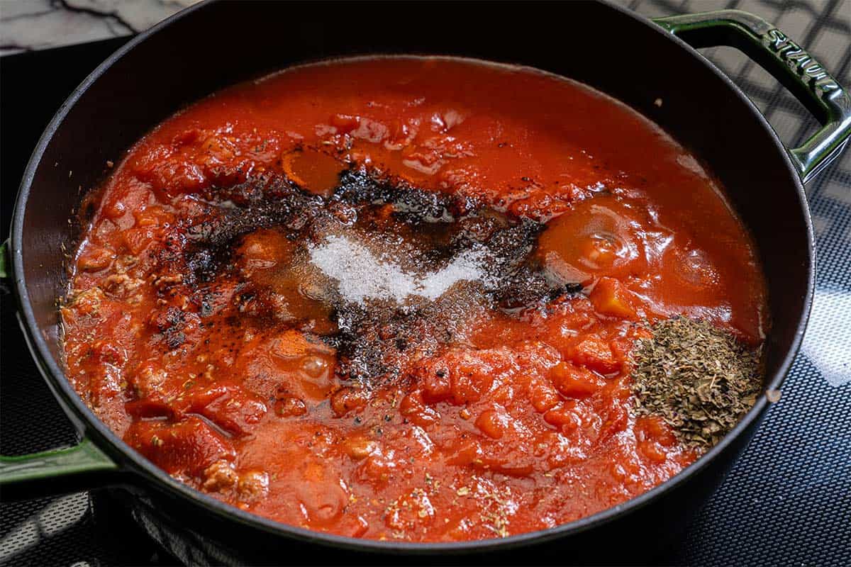 Image of passata being added and mixed into the sautéed vegetable and ground meat mixture in a pot.